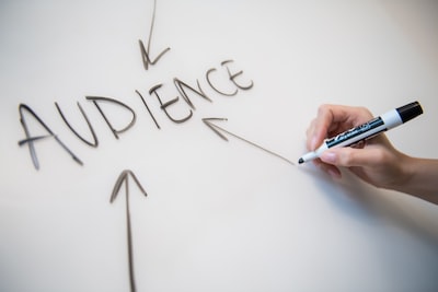 A person is writing the word 'AUDIENCE' on a whiteboard with arrows pointing towards it.